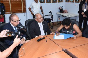 Foto de funcionaria con discapacidad firmando su designación en presencia del Director General