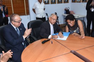Foto de funcionaria con discapacidad firmando su designación en presencia del Director General